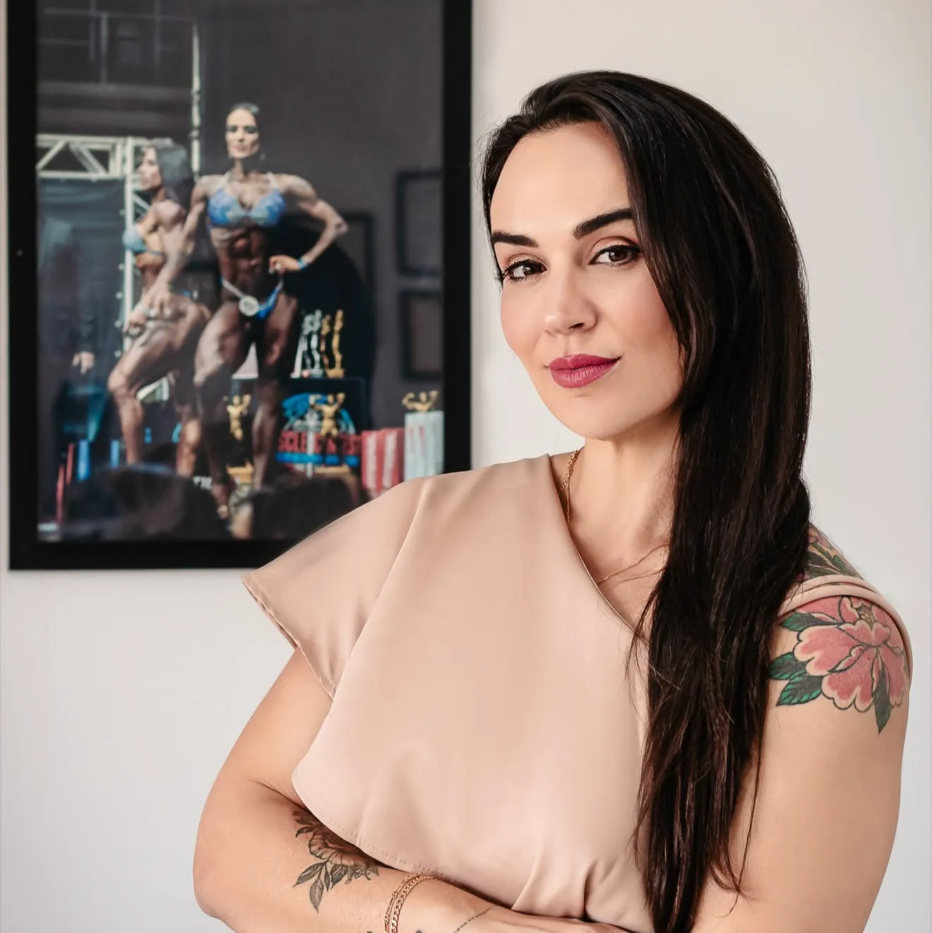 Patrícia Chiaverini de braços cruzados no consultório, com uma foto dela num palco de competição ao fundo