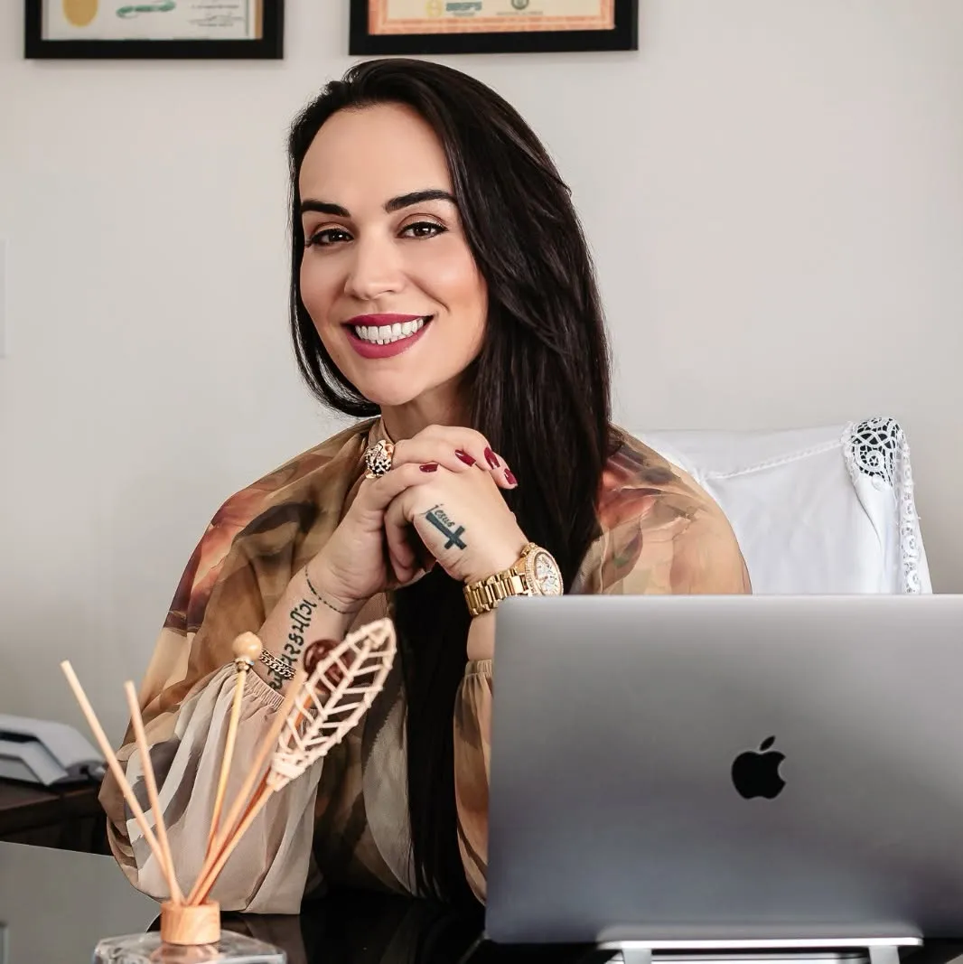 Patrícia Chiaverini sorrindo à mesa do consultório, com o notebook aberto